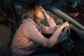 A blonde sad woman is sitting behind the wheel of a left-hand drive car and holding her head in despair, covering her Royalty Free Stock Photo