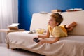 Blonde schoolboy boy plays video games, holds a gamepad, eats popcorn instead of learning lessons on blue background Royalty Free Stock Photo