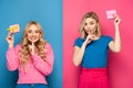 Blonde sisters holding gift boxes and showing silence sign on blue and pink background Royalty Free Stock Photo