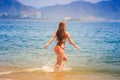 blonde slim girl in bikini runs into sea splashes against hills Royalty Free Stock Photo