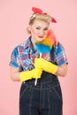 Blonde smiles with leer. Pretty housewife with pretty smile. Young lady with duster on rose background.