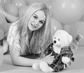Blonde on smiling face relaxing with teddy bear toy. Woman cute celebrate birthday with balloons. Girl in pajama