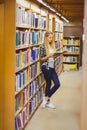 Blonde student reading book next to bookshelf Royalty Free Stock Photo