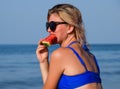 A blonde in sunglasses eats a watermelon by the sea. A juicy watermelon in the hands of a woman Royalty Free Stock Photo