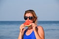 A blonde in sunglasses eats a watermelon by the sea. A juicy watermelon in the hands of a woman Royalty Free Stock Photo