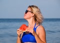 A blonde in sunglasses eats a watermelon by the sea. A juicy watermelon in the hands of a woman Royalty Free Stock Photo