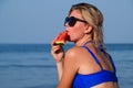 A blonde in sunglasses eats a watermelon by the sea. A juicy watermelon in the hands of a woman Royalty Free Stock Photo
