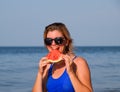 A blonde in sunglasses eats a watermelon by the sea. A juicy watermelon in the hands of a woman Royalty Free Stock Photo