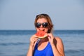 A blonde in sunglasses eats a watermelon by the sea. A juicy watermelon in the hands of a woman Royalty Free Stock Photo