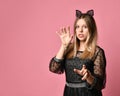 Teen girl in black dress, headband in form of cat ears, bracelet. Acting like she is a pussy, posing on pink background. Close up