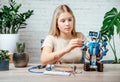 A blonde teen girl building and programming robot while studying robotics engineering and coding