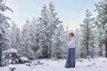 Blonde teen girl white knitted sweater long blue skirt stands beautiful snowy winter forest Park fir trees Royalty Free Stock Photo