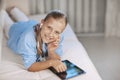 Blonde teenage girl lying on the couch plays a game on the tablet and communicates via video link with friends. Digital Royalty Free Stock Photo