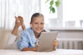 Blonde teenage girl lying on the couch plays a game on the tablet and communicates via video link with friends. Digital Royalty Free Stock Photo