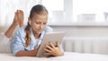 Blonde teenage girl lying on the couch plays a game on the tablet and communicates via video link with friends. Digital Royalty Free Stock Photo