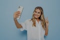 Blonde teenage girl showing peace sign while taking selfie on smartphone Royalty Free Stock Photo