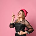 Teenage girl in sunglasses, black dress and red hat. She pointing at something by forefinger, posing on pink background. Close up Royalty Free Stock Photo