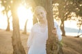 Blonde teenage girl in white shirt standing near tree on the background of sea Royalty Free Stock Photo