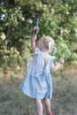 Blonde three years old girl with two tails and summerdress plays badminton. Child in blue dress holds racket and shuttlecock.
