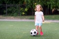 Blonde toddler girl in blue shorts and pink sneakers playing with soccer ball at football field or stadium outdoors. Girl power Royalty Free Stock Photo