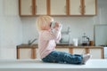Blonde toddler sits in kitchen and drinks from big cup. Breakfast at home