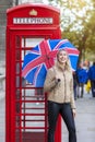 A blonde tourist with a english flag umbrella in her hand stands in front of a traditional, red telephone booth in London Royalty Free Stock Photo