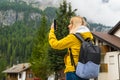 Blonde tourist takes photos using smartphone of misty Alpine mountains