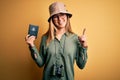 Blonde tourist woman with blue eyes on vacation holding australian passport using binoculars surprised with an idea or question