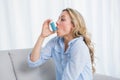 Blonde using her asthma inhaler on couch