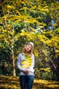 Blonde in white shirt and hat walks in beautiful park on sunny autumn day. Young pretty woman holds a branch with yellow leaves in Royalty Free Stock Photo