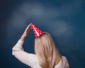 Celebrating a birthday or New Year. Middle aged woman holding a red party cone hat on her head. View from the back. Dark blue Royalty Free Stock Photo