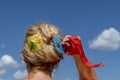 A blond woman arranges her hair using two colored paper umbrellas and a red ribbon, against the blue sky Royalty Free Stock Photo