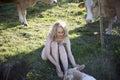 Blonde woman bends over to scratch the head of a white dairy cow lying in a green field