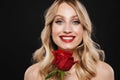 Blonde woman with bright makeup red lips posing isolated over black wall background holding rose flower Royalty Free Stock Photo