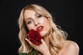 Blonde woman with bright makeup red lips posing isolated over black wall background holding rose flower Royalty Free Stock Photo