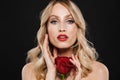 Blonde woman with bright makeup red lips posing isolated over black wall background holding rose flower Royalty Free Stock Photo