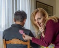 Blonde woman caught in the act while sticking a paper fish for April fools day behind a man, brings her index finger to her mouth