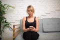 Blonde woman checking e-mail in internet via mobile phone, sitting on comfortable sofa in home room. Royalty Free Stock Photo