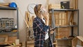 Blonde woman converses on a phone in a carpentry workshop while holding a tablet Royalty Free Stock Photo
