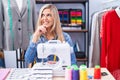 Blonde woman dressmaker designer using sew machine thinking worried about a question, concerned and nervous with hand on chin