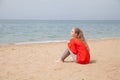 Beautiful blonde woman on an empty beach by the sea sits on the sand Royalty Free Stock Photo