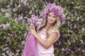 Blonde woman enjoying in a spring garden with blooming lilacs with bouquet, lilac flowers hair style.