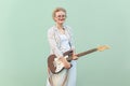 Blonde woman with eyeglasses, holding guitar and looking at camera with smile.