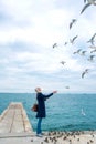 Blonde woman feeding seagulls in cloudy autumn day Royalty Free Stock Photo