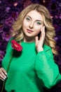 Blonde woman with a gentle make-up that looks at the camera while holding flower near the face on a floral background. Royalty Free Stock Photo