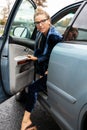 Blonde woman in glasses look back over her shoulder as she exits parked blue car in which she drove. Royalty Free Stock Photo