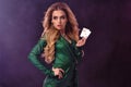 Blonde woman in green stylish dress and jewelry. Showing two playing cards, hand on waist, posing on purple smoky Royalty Free Stock Photo