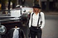 Blonde woman in hat and in black retro clothes near old vintage classic car Royalty Free Stock Photo