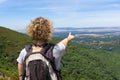 Blonde woman on her back with a backpack on her back, on top of a mountain, pointing with her hand to a valley