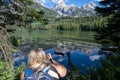 Blonde woman hiker kneels down to photograph Taggart Lake in Grand Teton Natinoal Park Royalty Free Stock Photo